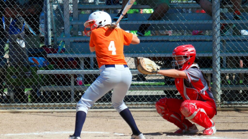 a softball player batting in an orange jersey